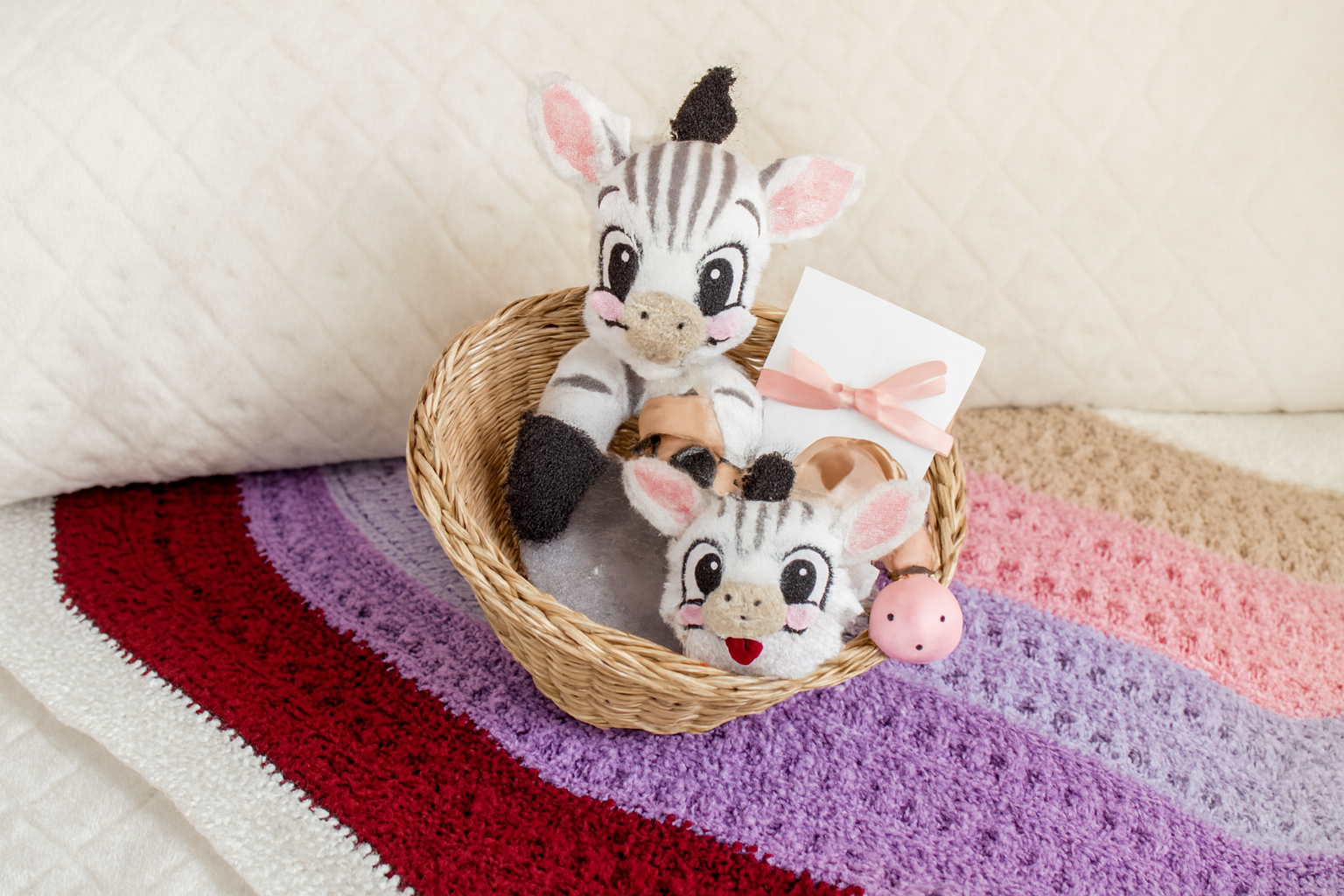 Panier cadeau artisanal posé sur une couverture crochetée, contenant un doudou zèbre et une attache-sucette assortie, idéal pour un kit naissance fait main.