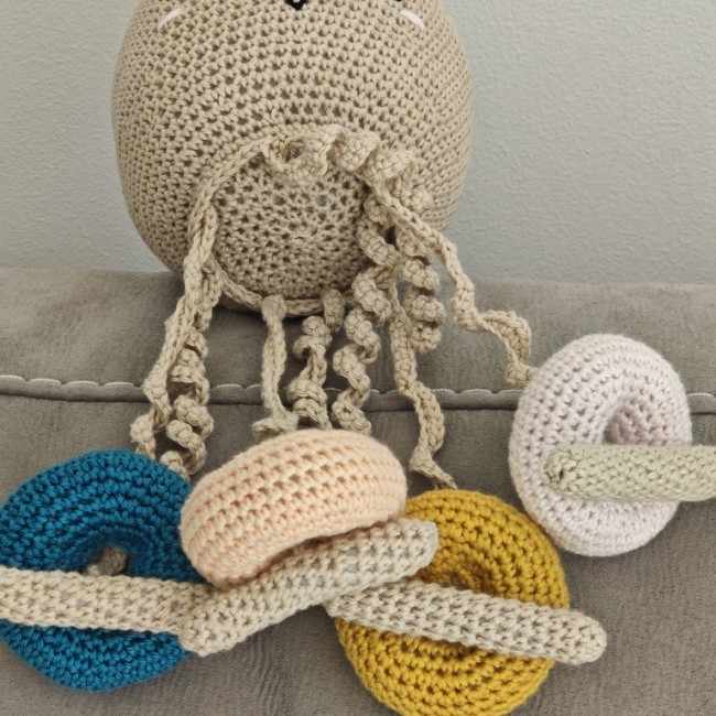 Pieuvre d’éveil au crochet beige tenant quatre anneaux colorés