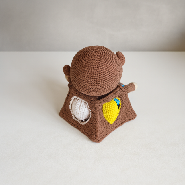 Singe en crochet assis sur fond bleu avec quatre balles colorées, jouet artisanal fait main