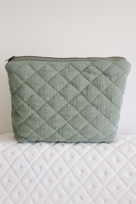 Trousse matelassée vert sauge avec fermeture zippée, posée sur fond blanc en tissu texturé