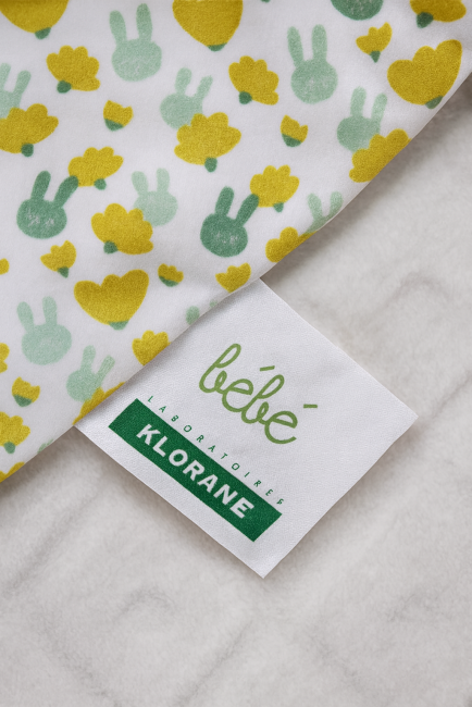 Tissu bébé blanc avec motifs verts et jaunes, nuages et lapins, étiquette Klorane