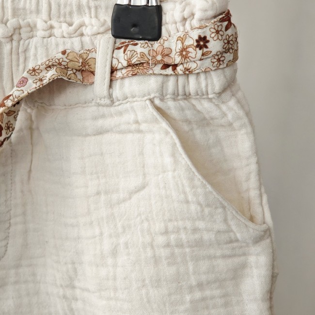 Pantalon léger 2 ans – tissu gaufré crème et cordon fleuri Détail du pantalon crème enfant avec lien fleuri et poche latérale