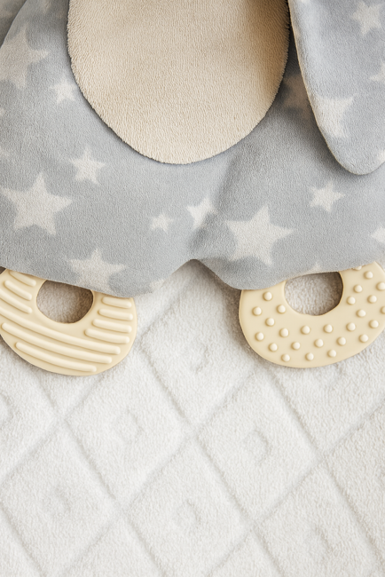 Doudou lapin gris étoilé avec anneaux de dentition texturés, sur couverture blanche 