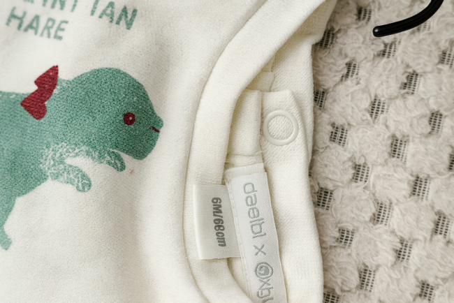 Étiquettes de taille et marque “oadiai x xiyou” sur sweat bébé, avec motif animal vert et texte “MOUNTAIN SHARE”.