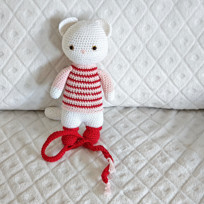 Moufette crocheté en coton avec écharpe rouge et bottines, yeux sécurisés, assis sur fond blanc texturé