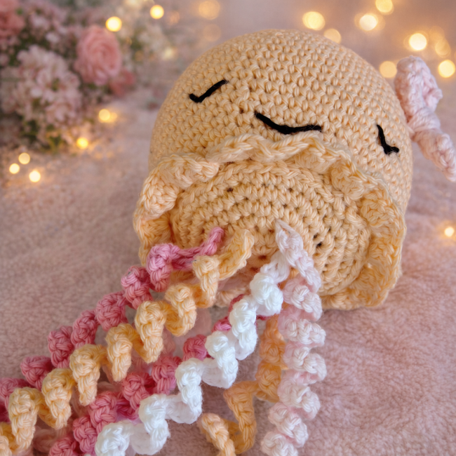 Pieuvre crocheté – douceur et poésie artisanale Pieuvre en crochet aux couleurs pastel, posé sur fond chaleureux avec roses et lumière tamisée