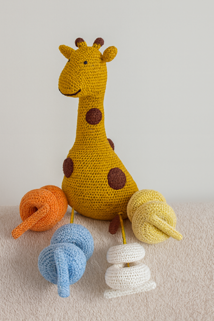 Girafe en crochet entourée de pelotes de laine colorées sur surface moelleuse