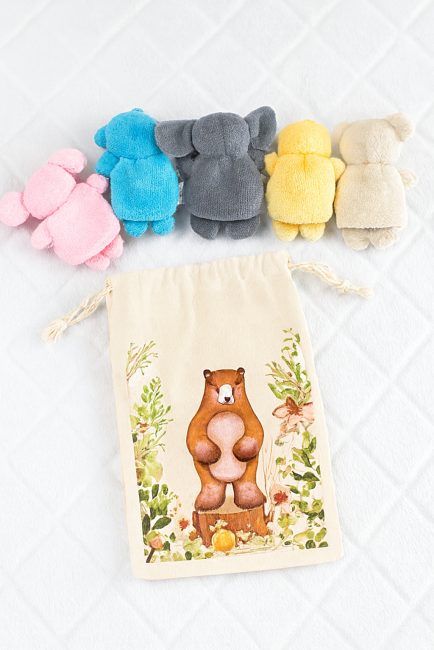Cinq petites marionnettes colorées alignées sur fond gris matelassé, accompagnées d’un sac tissu illustré.
