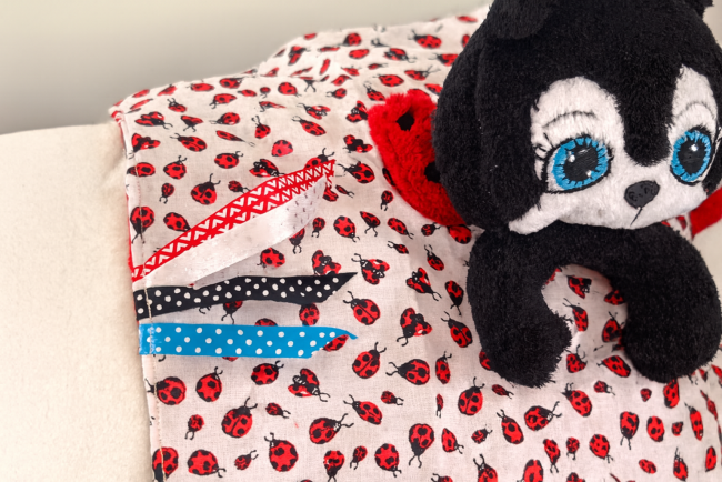 Peluche coccinelle noire et rouge posée sur tissu à motif coccinelles rouges et noires