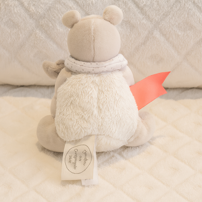 Doudou de seconde main – dos avec col à pois – Doudou et Compagnie Dos du doudou gris avec col blanc à pois et ruban rose, assis sur couverture matelassée