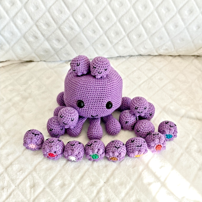 Pieuvre crochetée entourée de 16 bébés souriants, chacun orné d’une fleur colorée – jeu memory artisanal