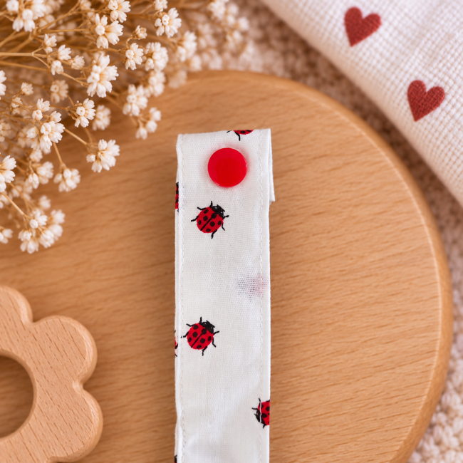 Détail de la pression rouge sur le tissu à coccinelles de l'attache sucette