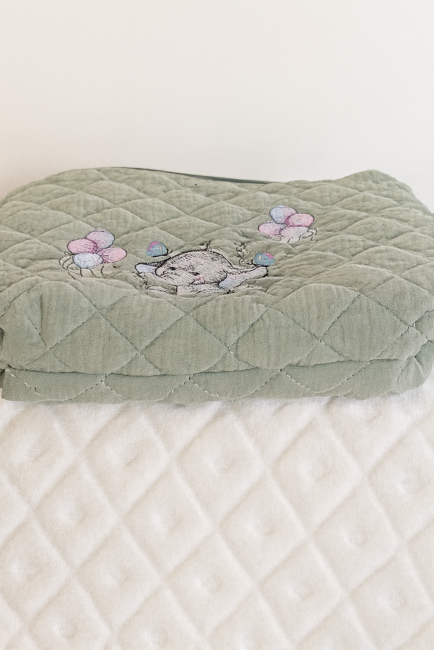 Trousse bébé vert matelassé avec broderie éléphant et ballons pastel, posé sur fond blanc texturé