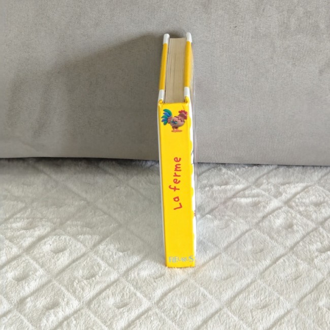 Tranche du livre cartonné « La ferme » – L’imagerie des bébés Tranche jaune du livre « La ferme » Fleurus, montrant le titre et l’illustration du coq.