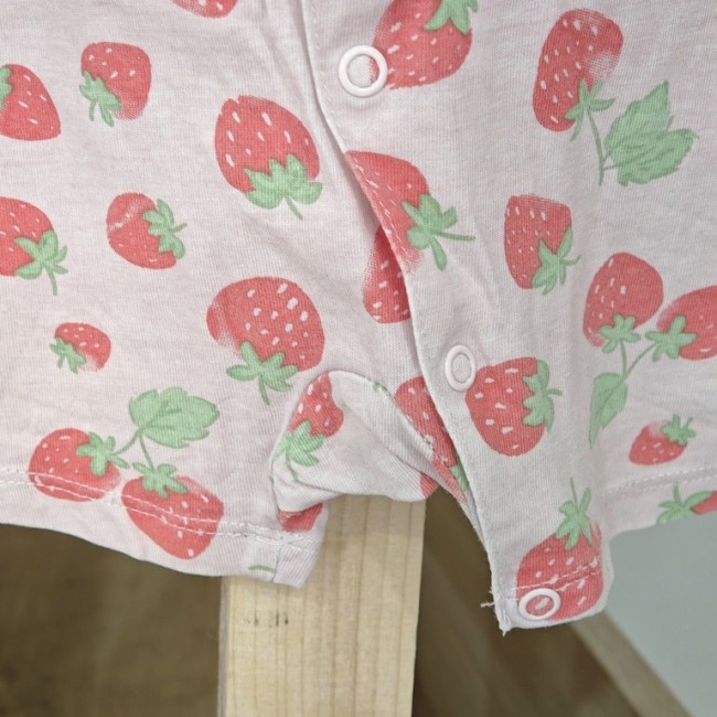 Boutons pression blancs sur tissu rose à motif fraises, détail du body bébé