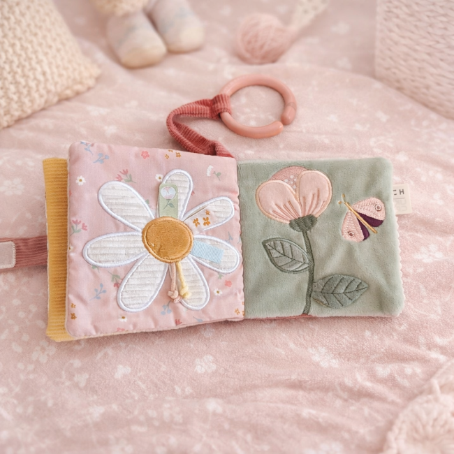 Livre d’éveil en tissu avec fleurs brodées rose et vert, posé sur surface matelassée pastel