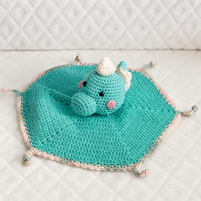 Doudou dinosaure crocheté avec tête en relief, yeux noirs et joues roses