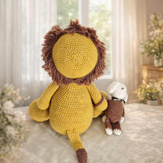 Doudou lion crochet moutarde tenant son petit lapin, vus de dos dans une ambiance douce et lumineuse.