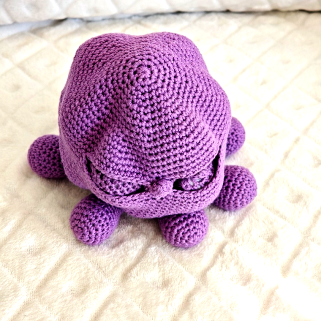 Pieuvre en crochet violette vue de dos, sur fond matelassé blanc