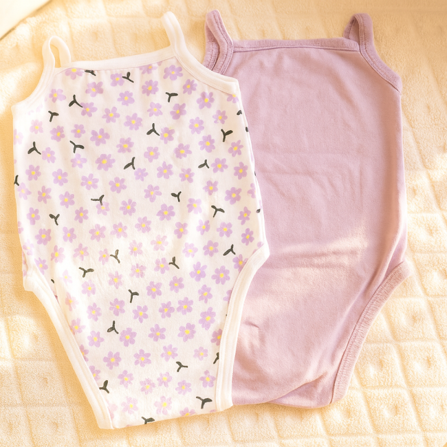 Lot bodys bébé fille 12M – tons mauves - vue de dos Bodys bébé sur fond crème tricoté