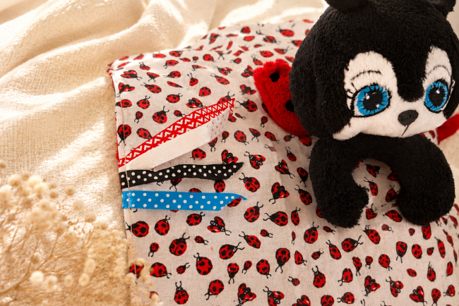 Peluche coccinelle artisanale – harmonie de motifs et textures Peluche coccinelle noire et rouge posée sur tissu à motif coccinelles rouges et noires