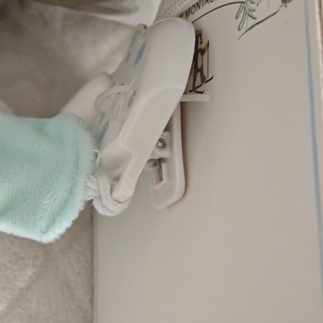 Clip de fixation blanc pour attache‑sucette, système sécurisé à pince, présenté sur fond doux sable vanille.