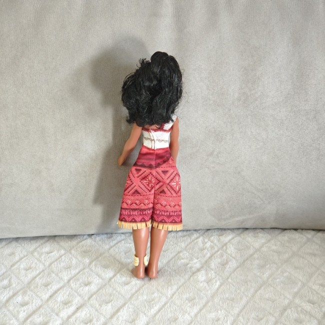 Poupée d’inspiration polynésienne montrée de dos, cheveux bouclés et jupe rouge à motifs