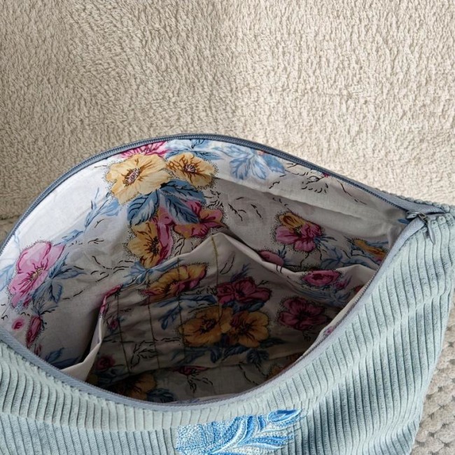 Vue intérieure d’une trousse en velours bleu avec doublure fleurie et poches de rangement Intérieur de trousse artisanale – Doublure fleurie et compartiments