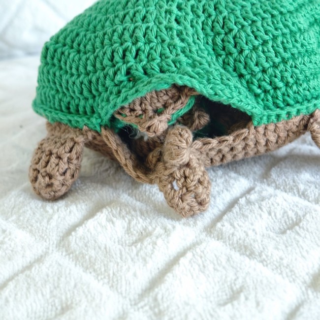 Tortue crochetée verte et brune posée sur une surface blanche