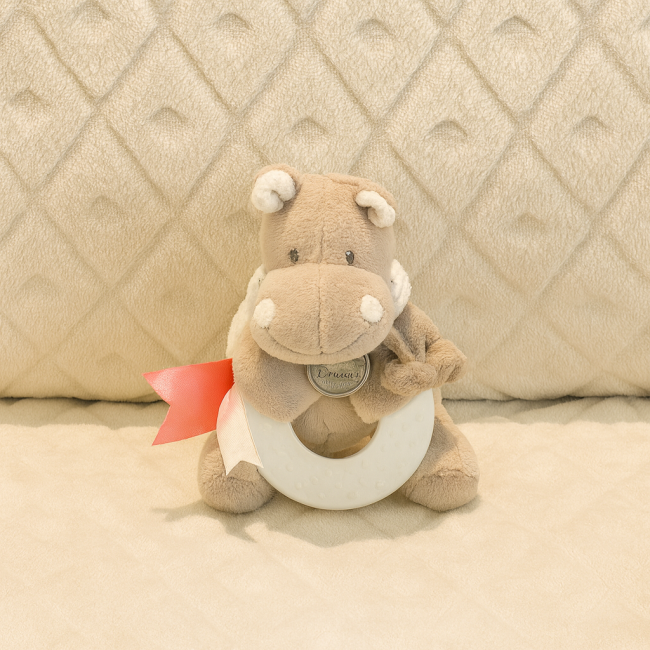 Doudou hippopotame seconde main – 12 cm – anneau de dentition et grelot intérieur Doudou hippopotame gris avec anneau de dentition blanc et ruban rose, assis sur couverture matelassée