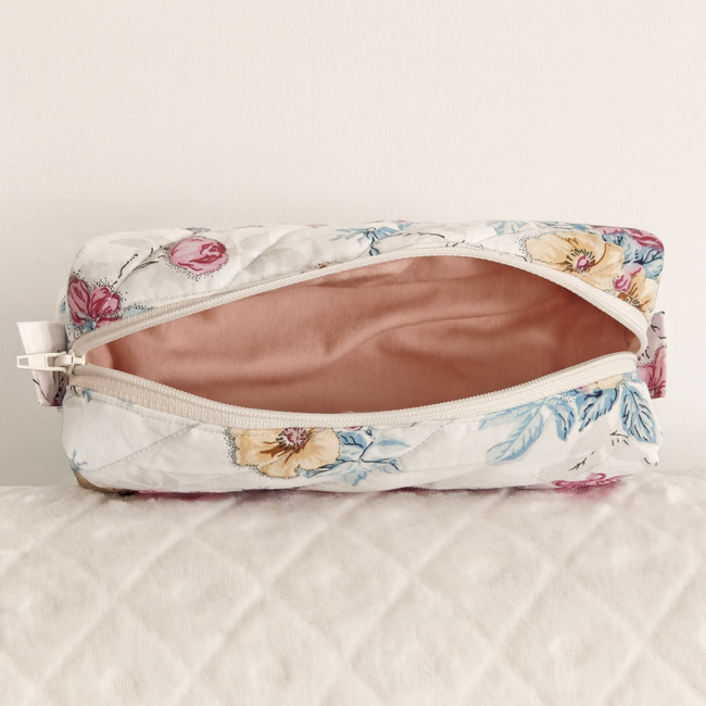 Trousse ouverte en tissu fleuri avec intérieur rose poudré, posée sur fond matelassé