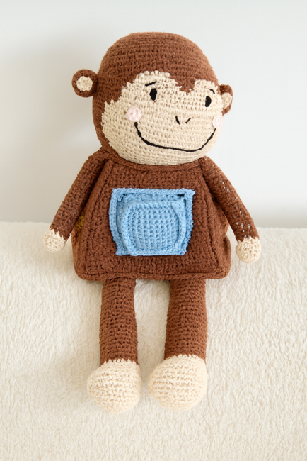 Singe en crochet vu de face avec patch bleu et accessoire, sur fond neutre