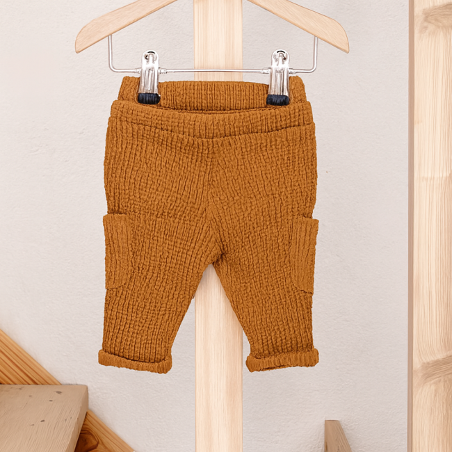 Pantalon bébé moutarde en tissu gaufré avec poches, suspendu sur cintre bois