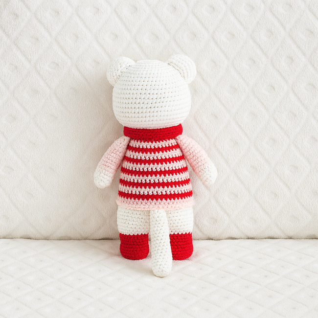 Doudou crocheté en coton avec lacets rouges et tenue rayée, yeux sécurisés, sur fond blanc texturé