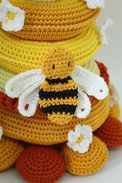 Jeu à empiler abeille – Création en crochet douce et pédagogique Abeille crochetée sur structure en couches jaune et orange avec fleurs blanches