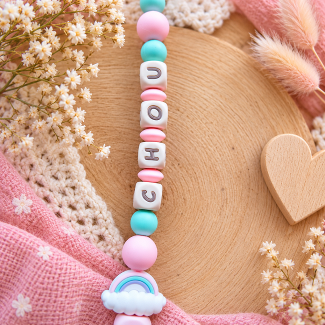 Gros plan sur l’arc-en-ciel en silicone rose et menthe et le cœur en bois naturel de l’attache sucette