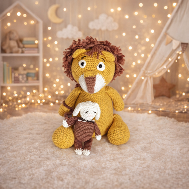  Doudou lion crochet moutarde avec petit lapin blanc et marron, posés sur un plaid dans une ambiance cosy et chaleureuse.