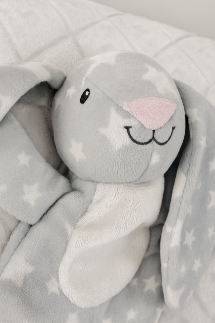 Doudou lapin gris à étoiles blanches, visage brodé et ventre blanc, sur fond matelassé