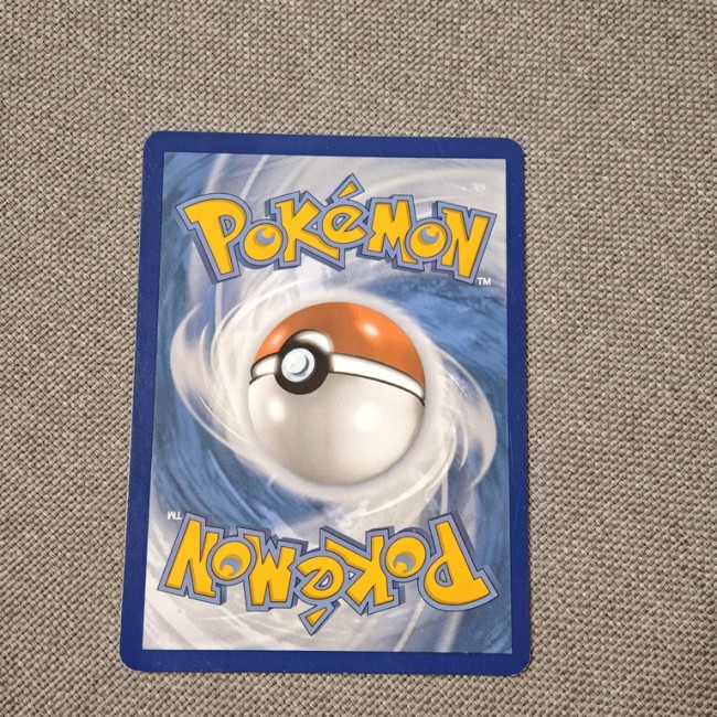 Dos d’une carte Pokémon officielle – design Poké Ball – fond bleu tourbillonnant – vue sur tissu gris