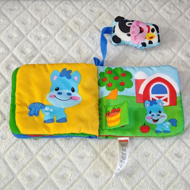 Livre tissu Fisher-Price – page cheval ferme Livre tissu Fisher-Price ouvert avec cheval bleu et jouet vache