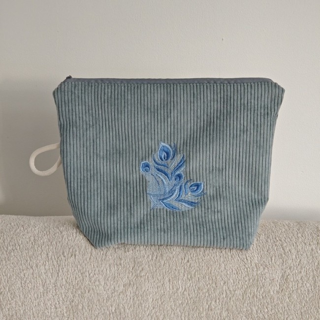 Trousse en velours côtelé bleu-gris avec broderie machine plume bleue, anse blanche sur le côté Trousse artisanale en velours bleu – Broderie plume