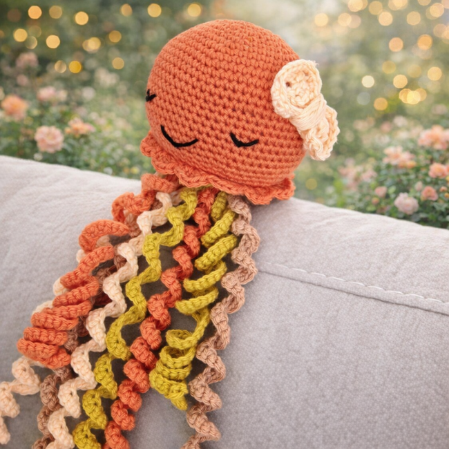Pieuvre en crochet orange avec noeud – création artisanale Bouille de Laine Pieuvre en crochet orange, posé sur un canapé gris dans une ambiance chaleureuse et décorative.