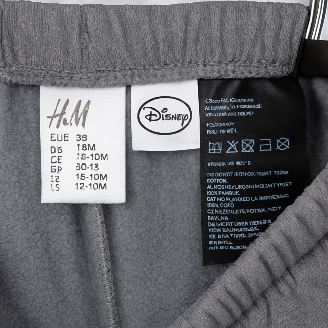 Détail des étiquettes du pantalon Disney Simba – H&M – 12-18 mois Étiquettes intérieures du pantalon bébé H&M x Disney, taille 12-18 mois, 100% coton