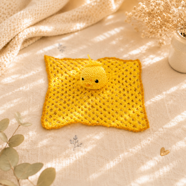 Petit poussin au crochet jaune posé sur un doudou ajouré fait main dans une décoration cocooning