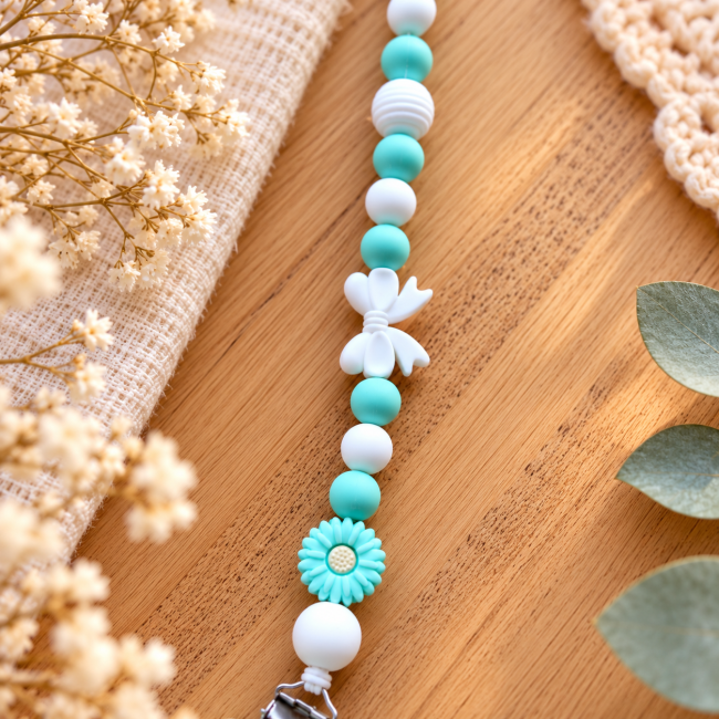 Gros plan sur les perles en silicone vert et blanc, le nœud blanc et la fleur décorative.