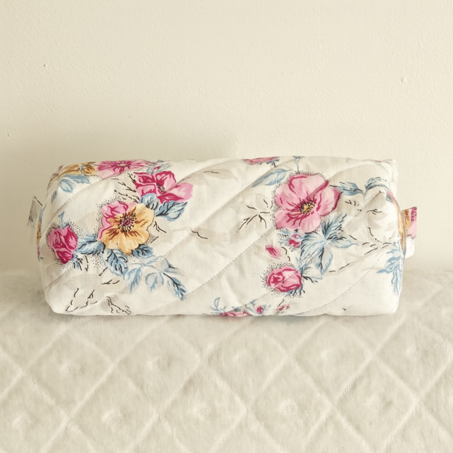 Trousse cylindrique matelassé fleuri posé sur surface blanche texturée