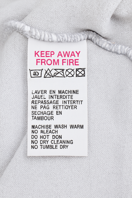 Étiquette d’entretien textile avec instructions en français et anglais, sur fond gris clair