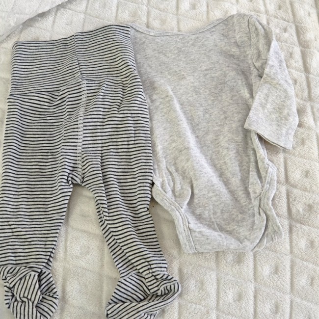 Tenue bébé avec body gris clair et pantalon à rayures noires et blanches, posée sur fond blanc matelassé.