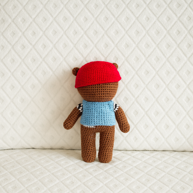 Vue arrière d’un ours en crochet avec casque rouge et pull rayé bleu et blanc 