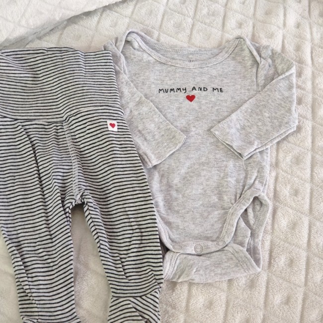Vêtements pour bébé posés sur couverture matelassée : body gris 